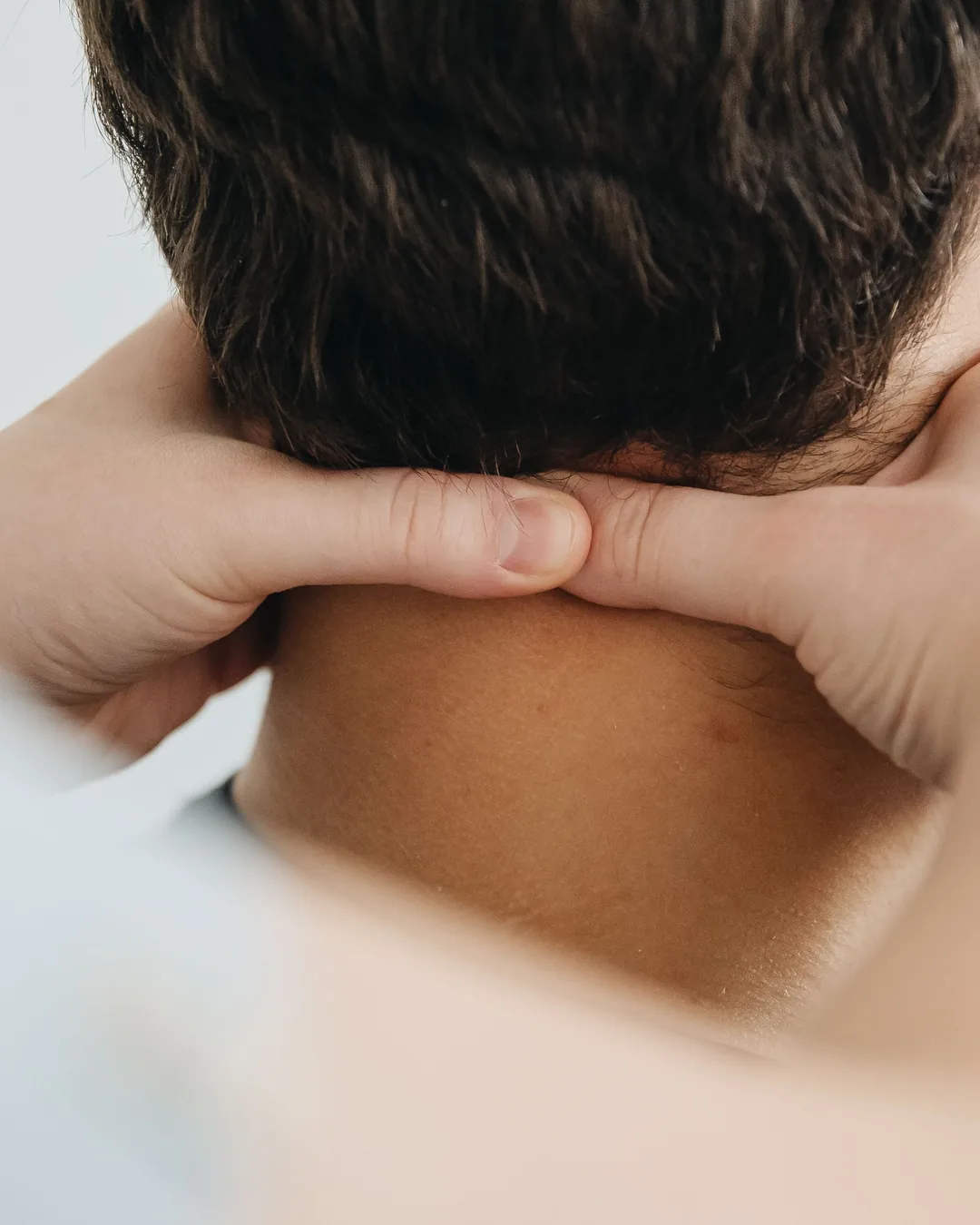 Les mains d'un praticien posées à la base du crâne, sur la nuque d'une personne vue de dos