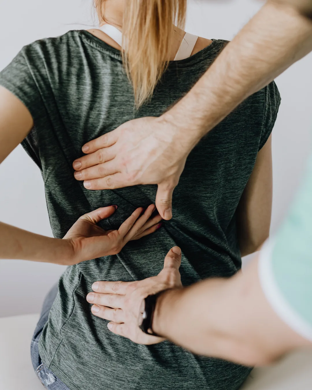 Les mains d'un praticien posées sur le bas du dos d'une personne assise : approche manuelle à domicile