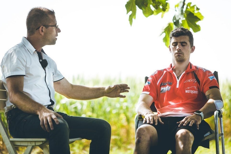 Séance de préparation mentale en extérieur avec Romain Berthomé, alors pilote de motocross et supercross : deux personnes assises face à face, l'une les yeux fermés